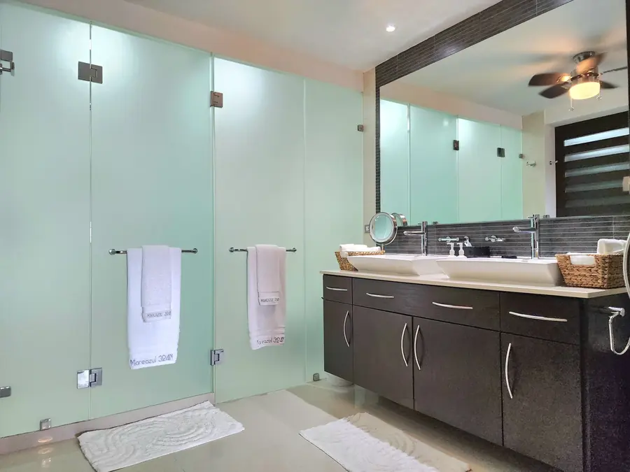 Kamar mandi dengan panel kaca frosted, handuk putih, dan wastafel ganda