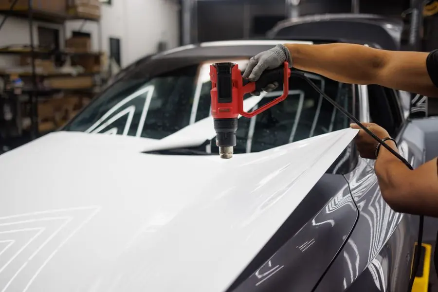 Tangan teknisi memasang film putih pada kap mobil dengan heat gun